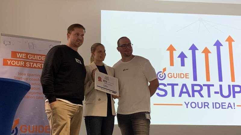 Katja Scheidler holding a certificate at the University of Duisburg-Essen startup idea competition, standing between two colleagues.